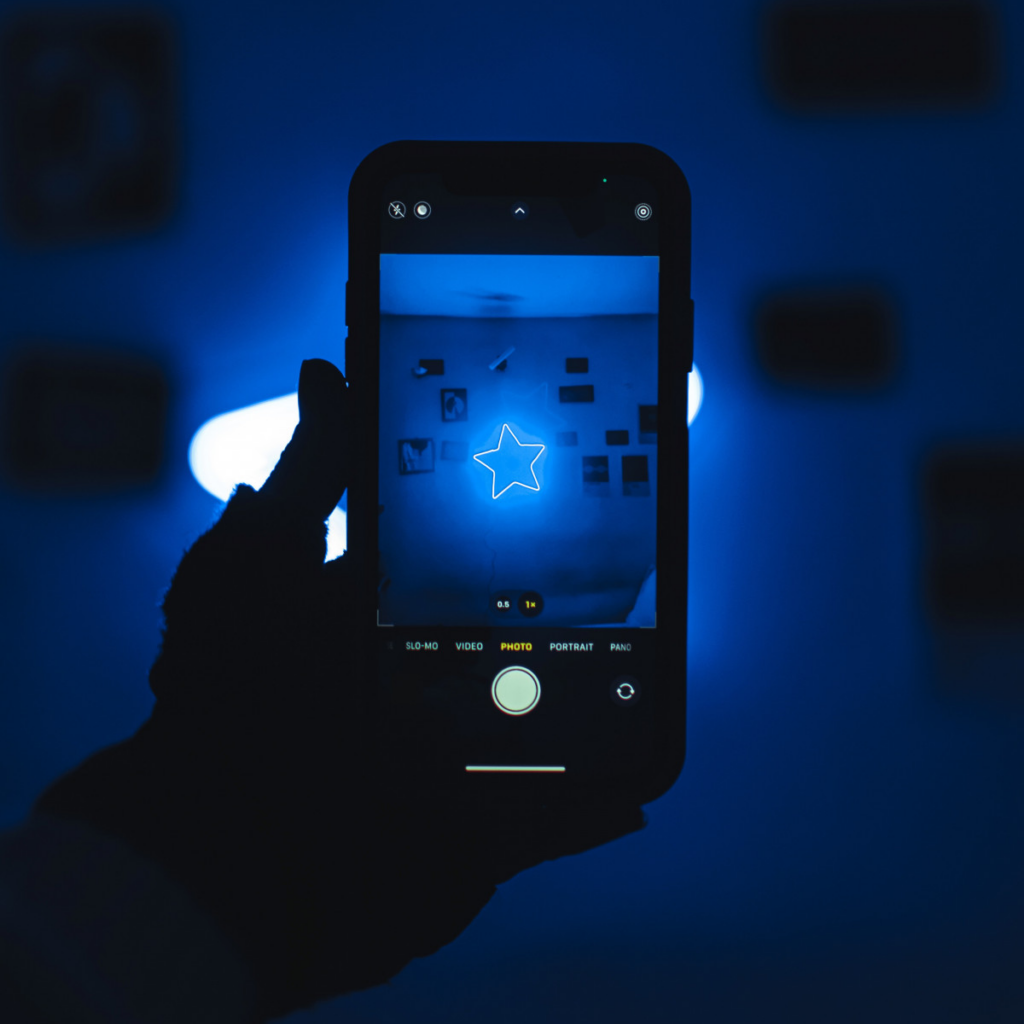 A person's hand holding up a phone with the camera app open with a blue start in the background that illuminates everything in blue, including picture frames.
